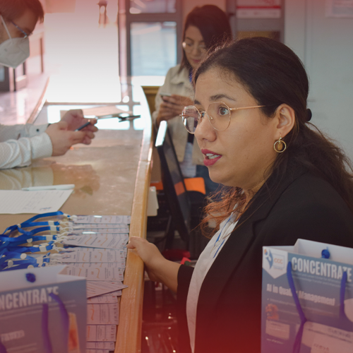 Sarah sitzt am Empfangscounter, Seitenportrait, sie spricht mit jemandem, der nicht zu sehen ist